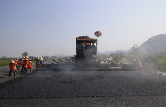 2019年8月，宜春經(jīng)開區(qū)S311路面攤鋪現(xiàn)場，工友們輔助路面兩側(cè)的分料、補(bǔ)窩等作業(yè)